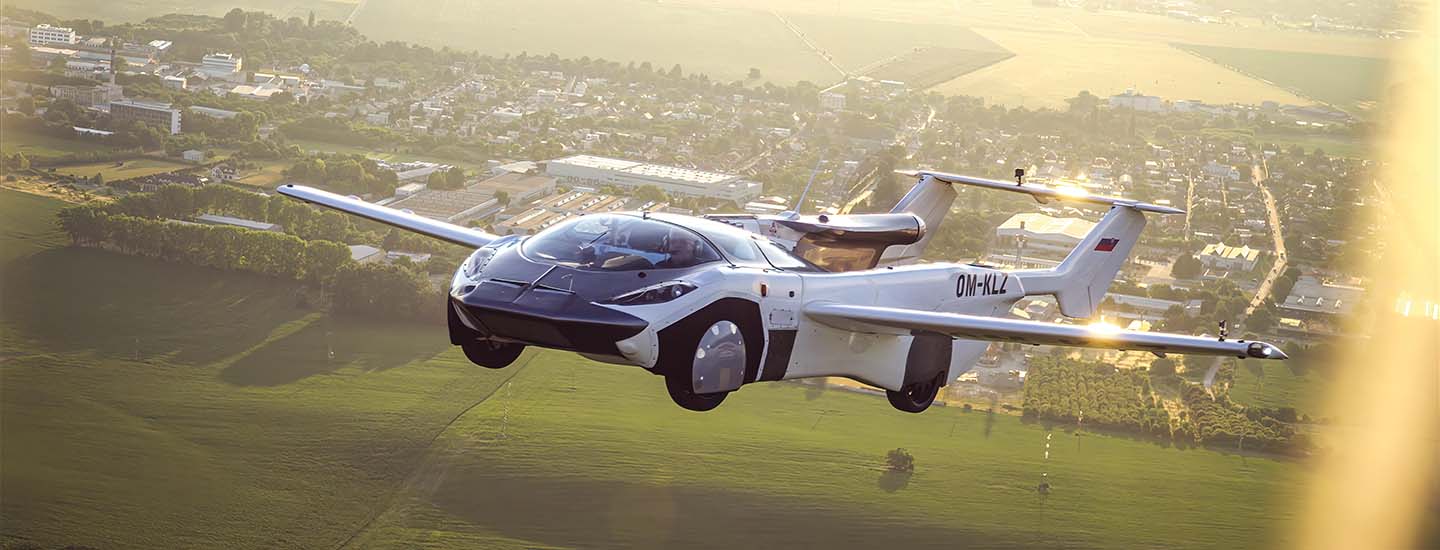 A car with airplane wings flying over green land